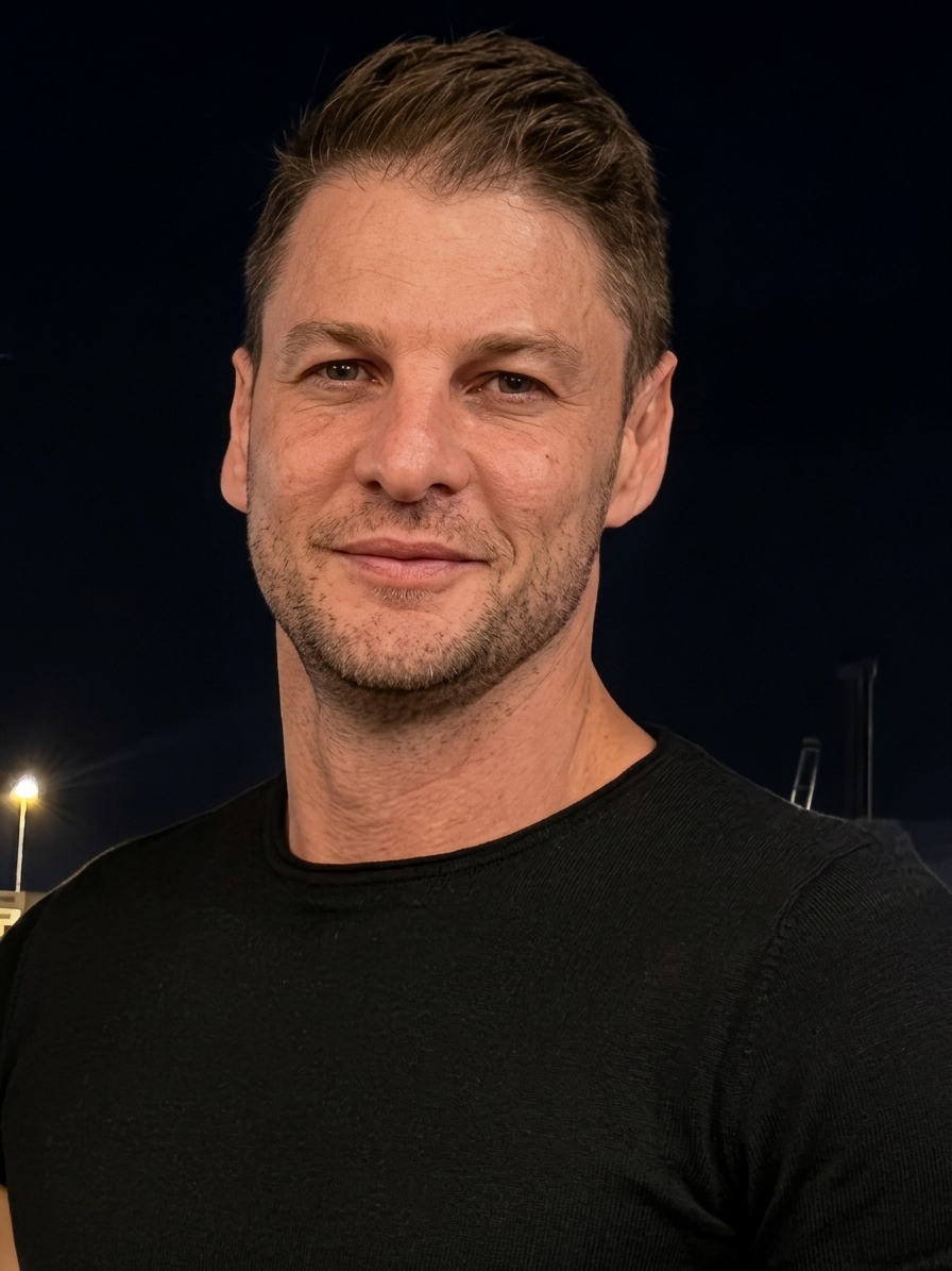 A man with short brown hair and light stubble wearing a black t-shirt
